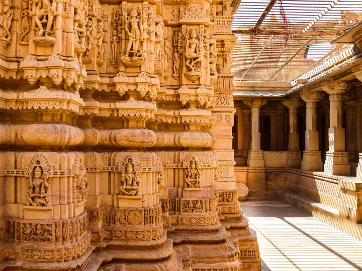 Beautiful stone carvings depicting historical Indian temple architecture with sunlight streaming through columns.